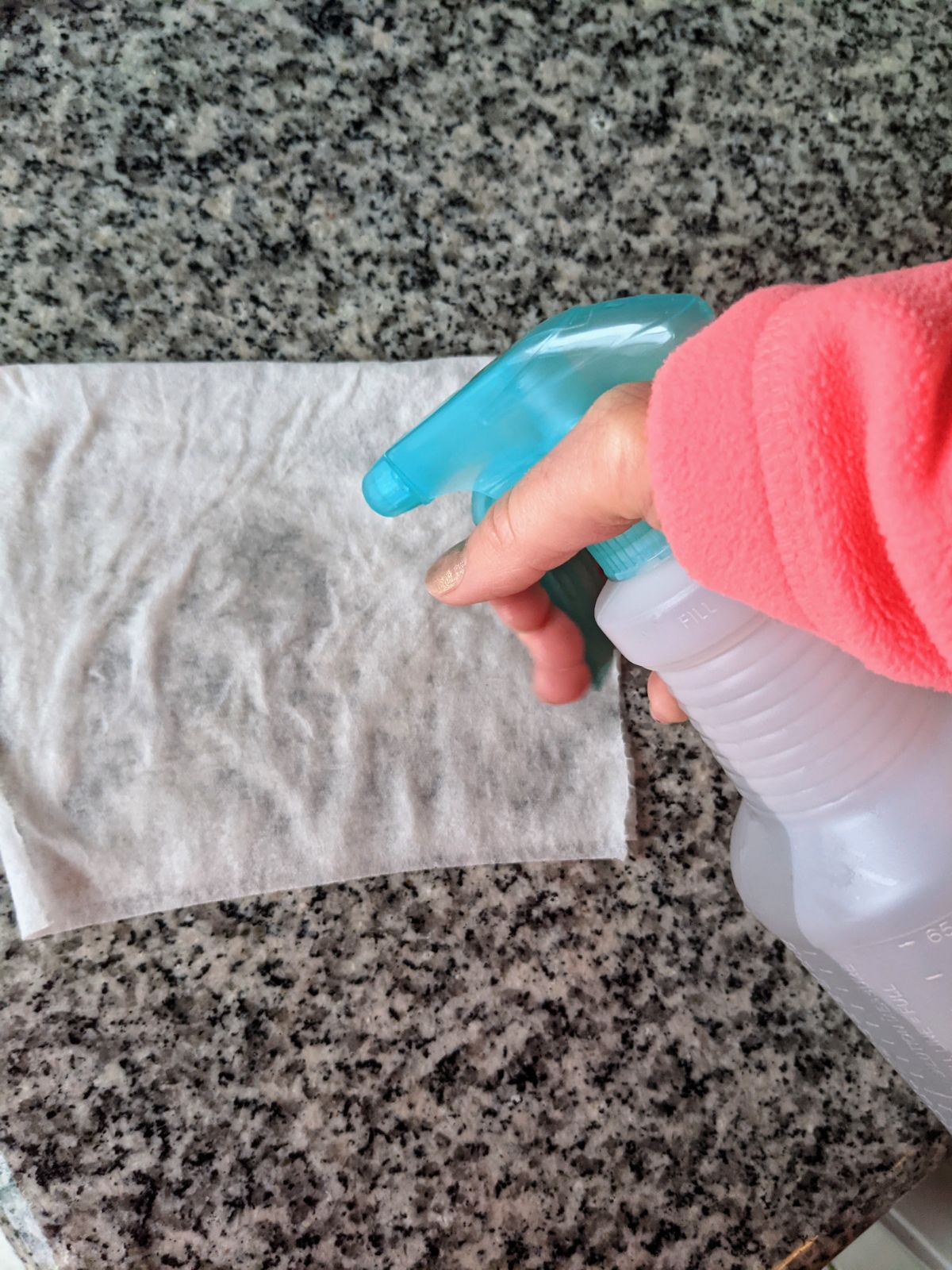 Woman's hand spraying a paper towel with tap water from a turquoise and white spray bottle
