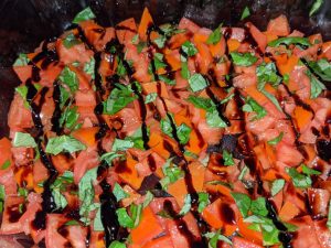 Balsamic Glaze on Roma Tomatoes and Fresh Basil Leaves in a Glass Pan