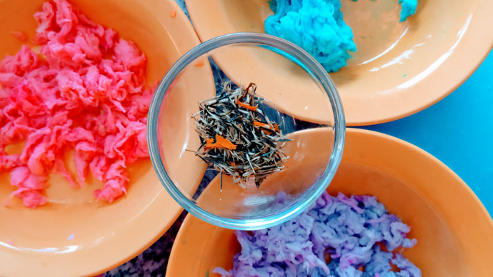 Three orange plastic bowls of bright colored dyed tissue and a dish of marigold seeds for making Plantable Art Seed Paper.