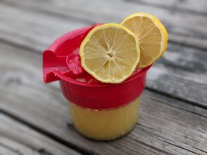 One Cup of Fresh Squeezed Lemon Juice in a Hand Juicer with Two Halves of a Sliced Lemon on a Wooden Deck