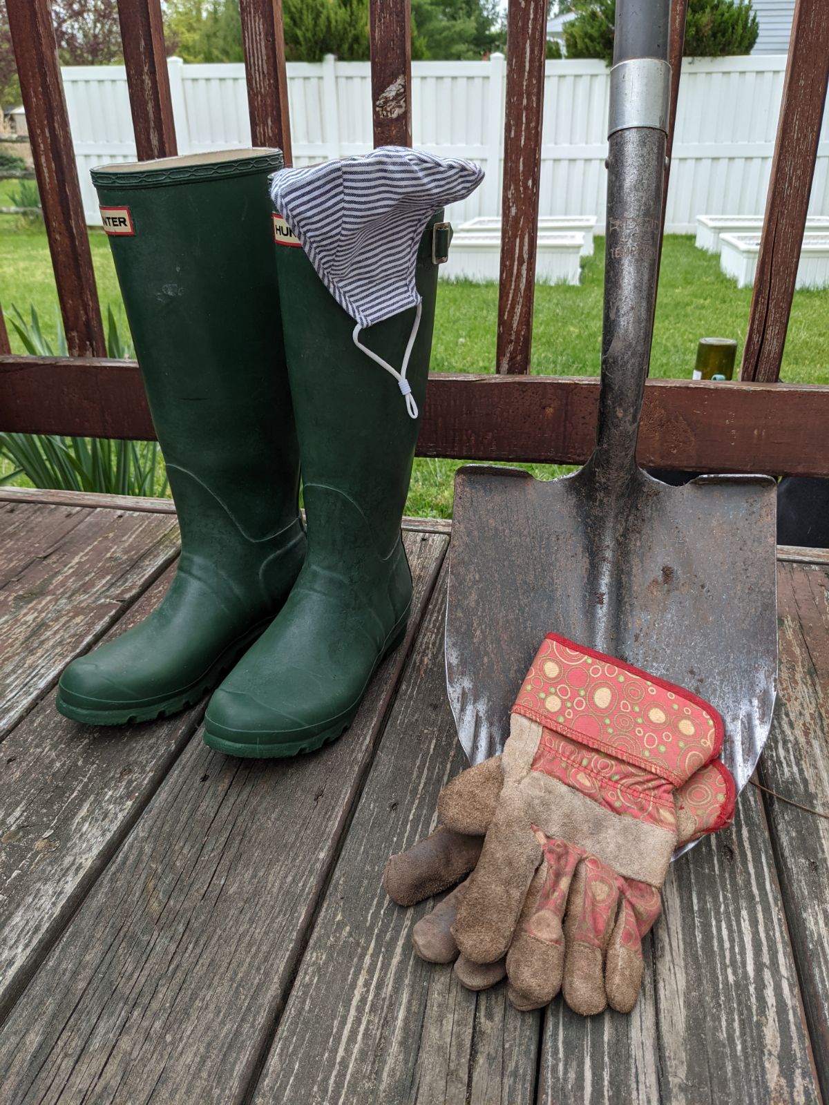 Protective gear to wear when removing poison hemlock - rain boots, thick garden gloves, and a mask next to a shovel