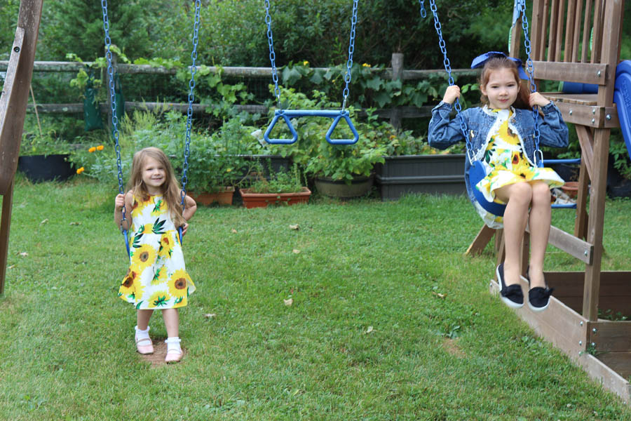 Girls in sunflower dresses on swing set by raised garden beds