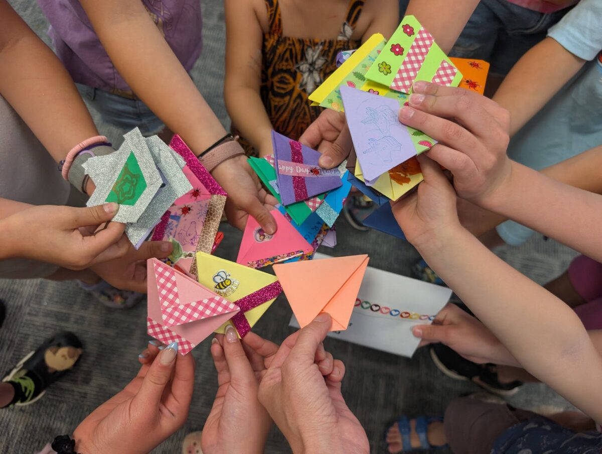 Kids holding hand-folded Origami seed packets in the center like a huddle