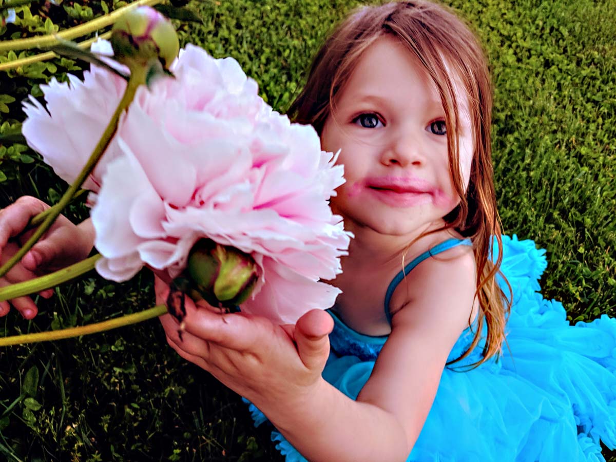 Daughter Holding Pink Fluffy Peony Flower in Garden in Blue Dress