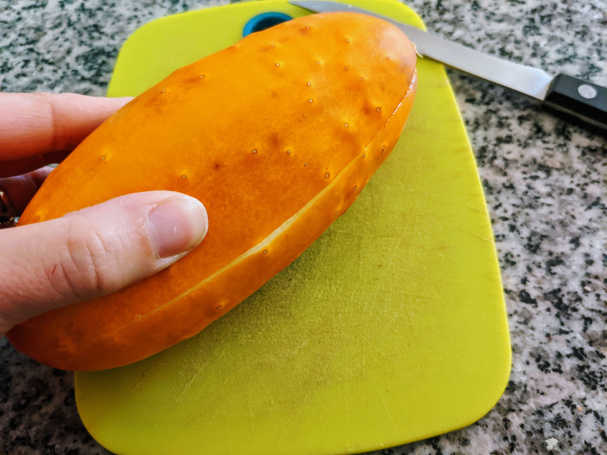 Pinch or Twist shallow-cut cucumber to reveal the seeds. Hand holding yellow cucumber.