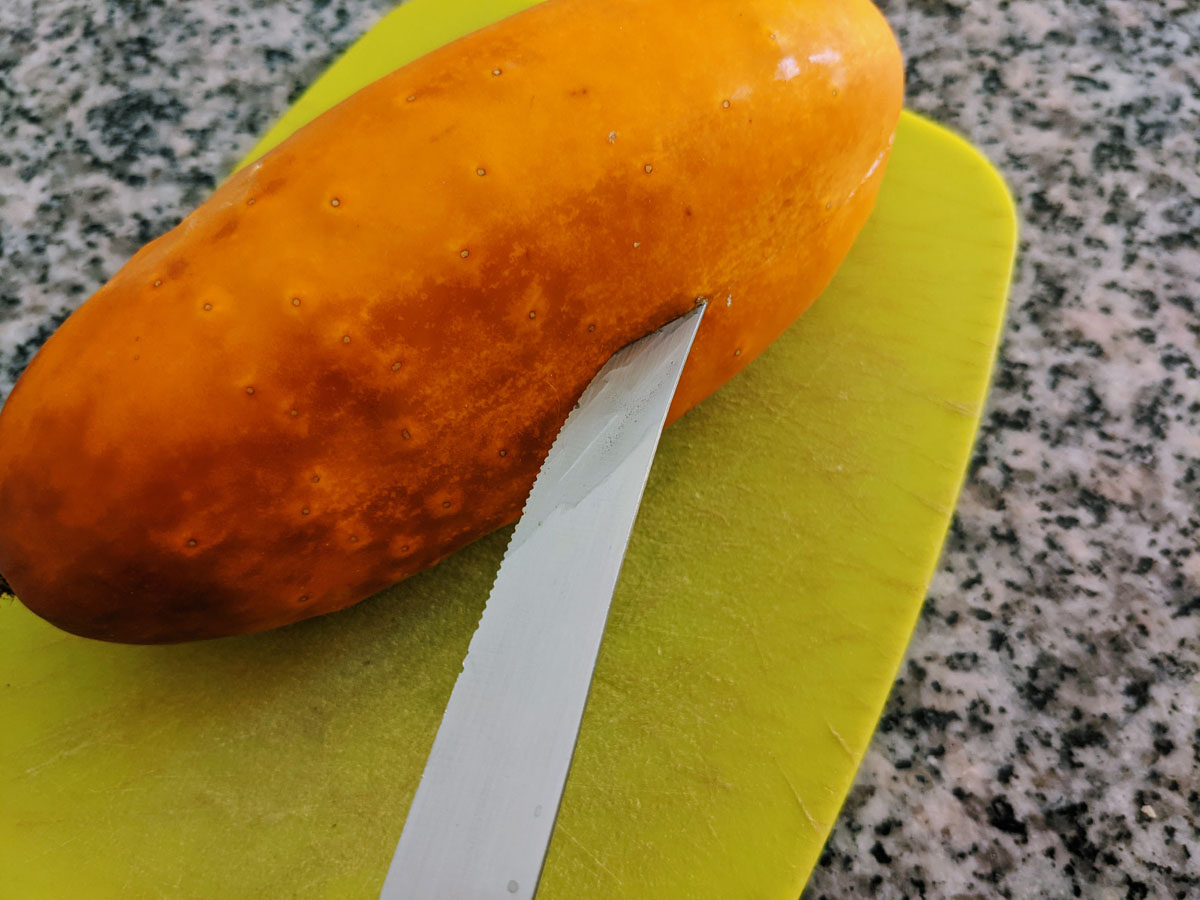 Shallow-cut a cucumber to save seeds - yellow cucumber with knife on cutting board