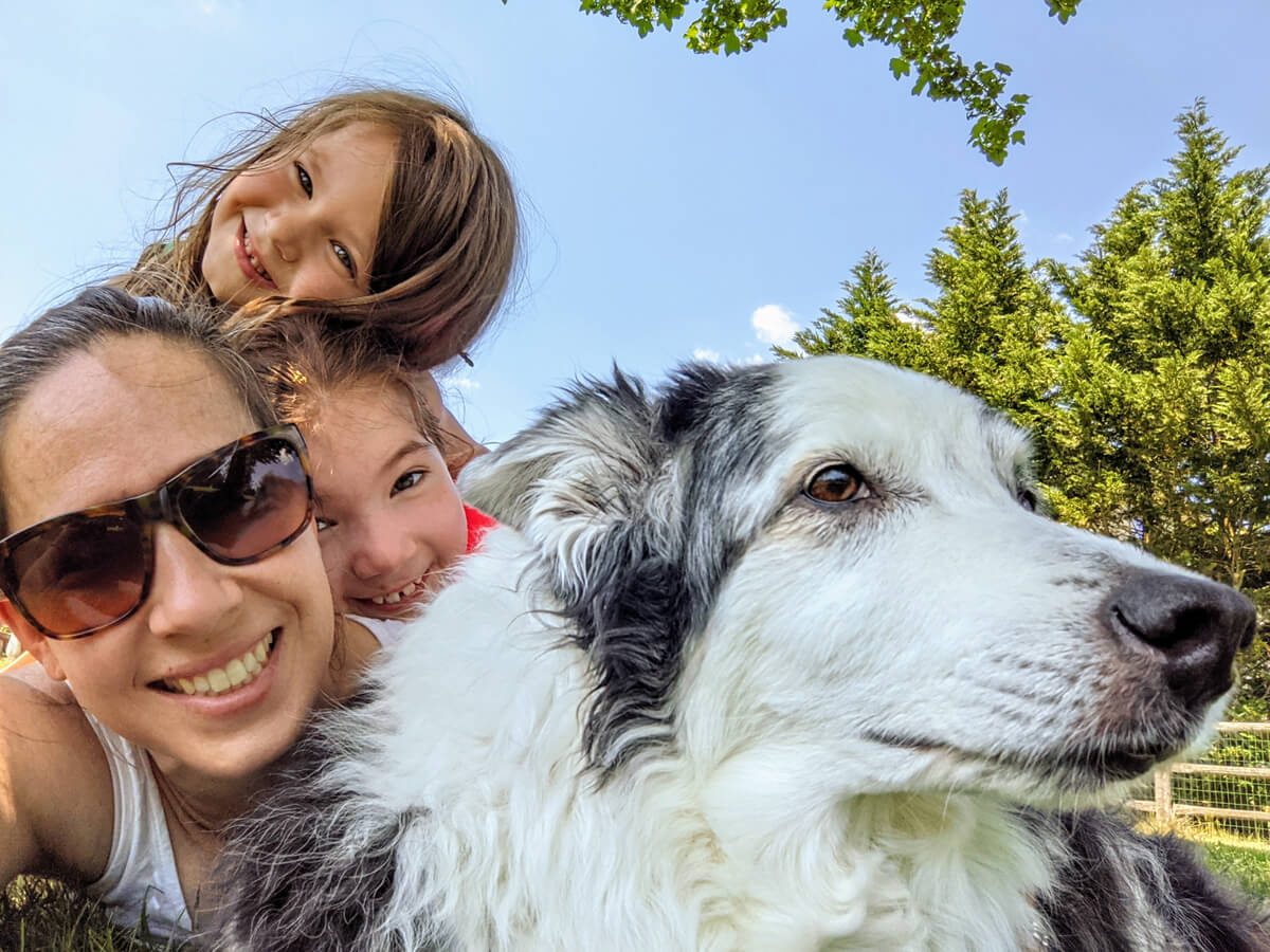Mom, Dog and two Daughters piled up outside under blue skies and trees