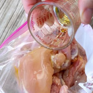 Drizzle Olive Oil on raw chicken thighs in plastic baggie