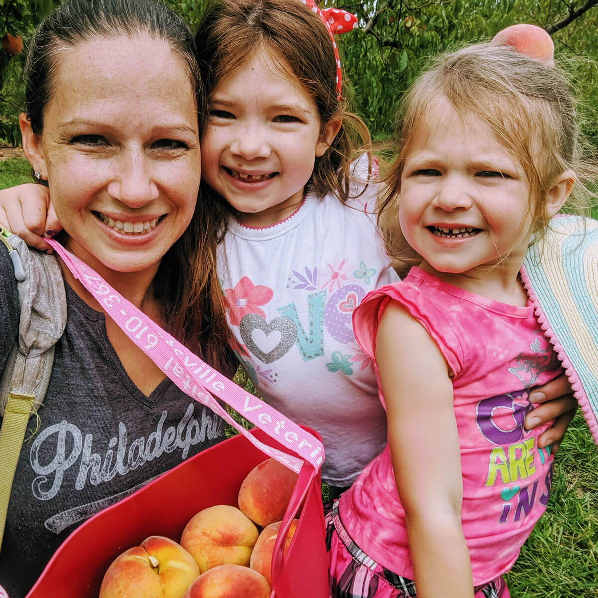 Mom and Daughters Picking Peaches in the Summer with a big red bucket of peaches