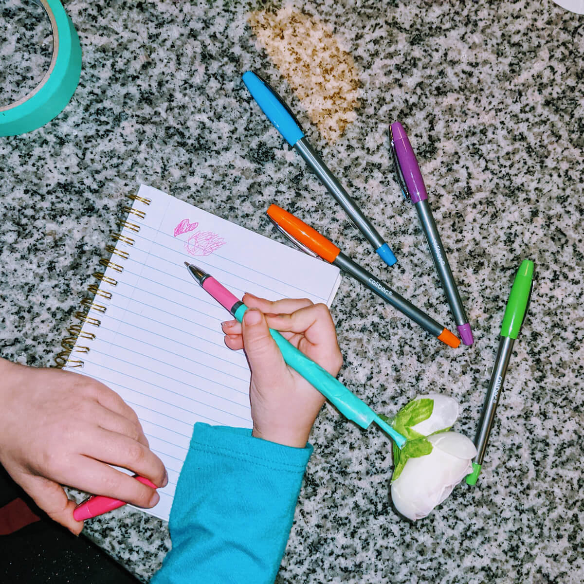 Little Girl Writing with a Flower Pen and other colored pens in a notebook