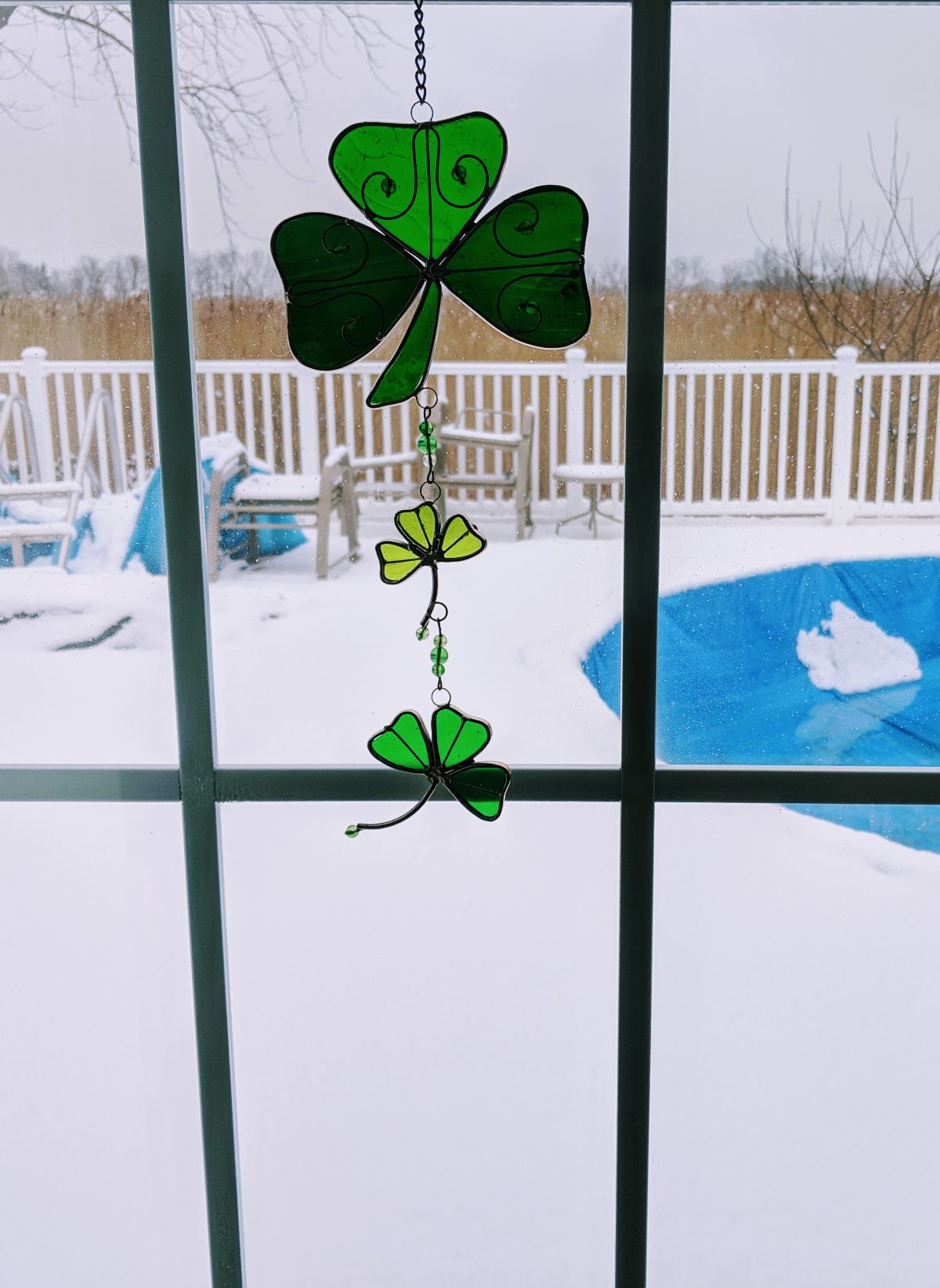 Shamrock suncatcher on glass door with snow on the deck around a pool in the background