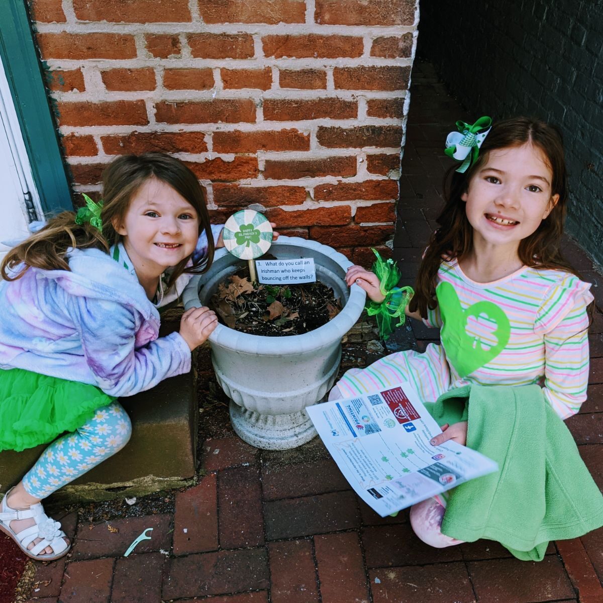 Daughters finding clues on a leprechaun hunt near a planter with a plant stake