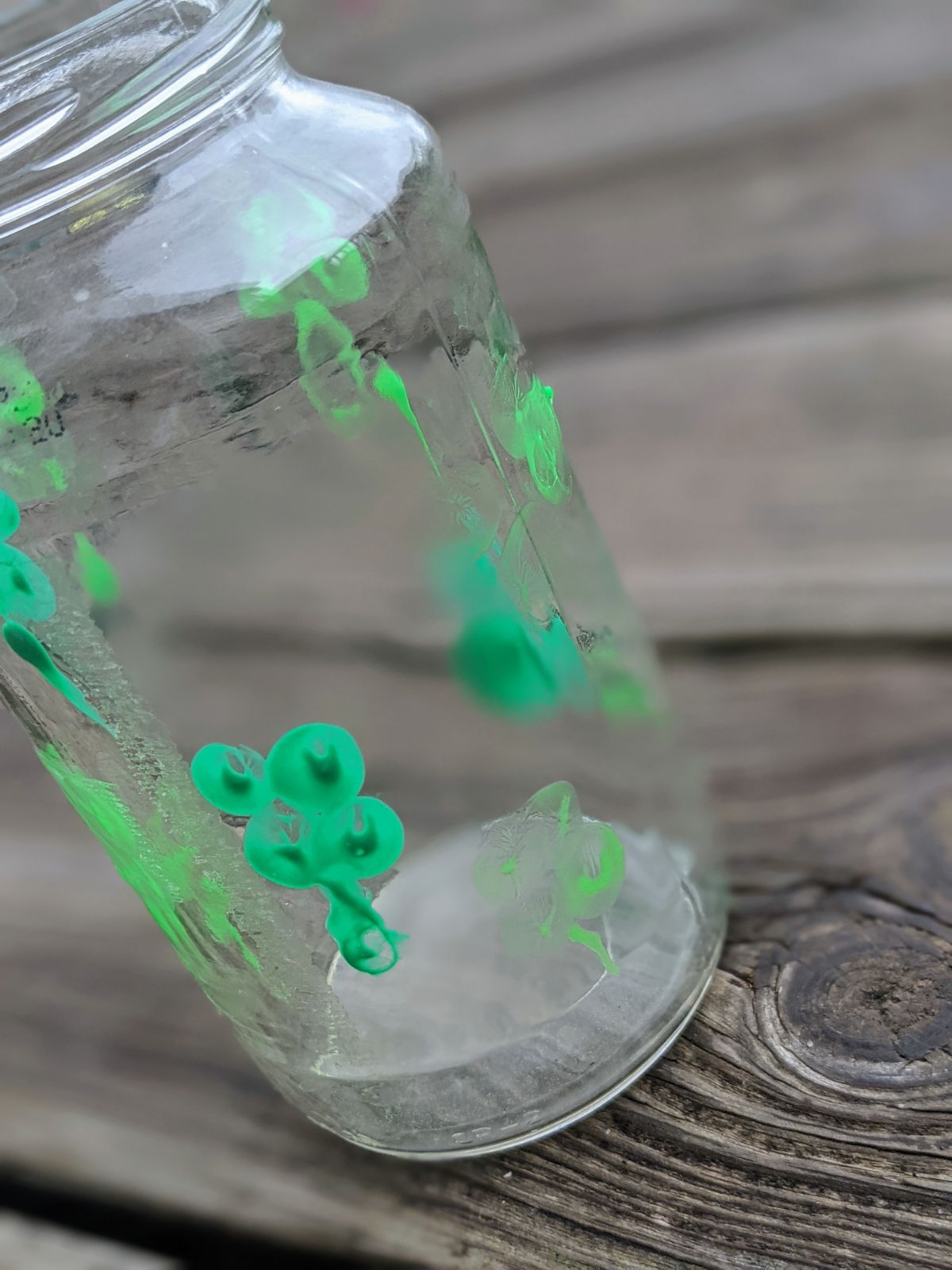 Glass jar shamrock vase with thumbprints made into four-leaf clovers outside on a wooden deck