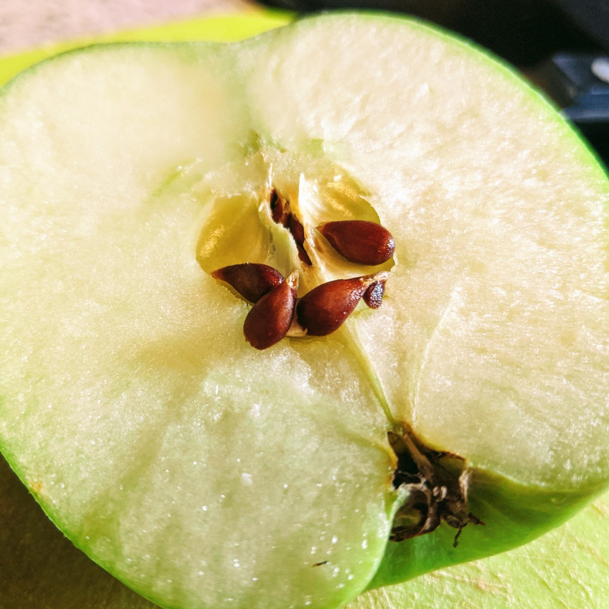 Many apple seeds falling out of a green apple half on a cutting board