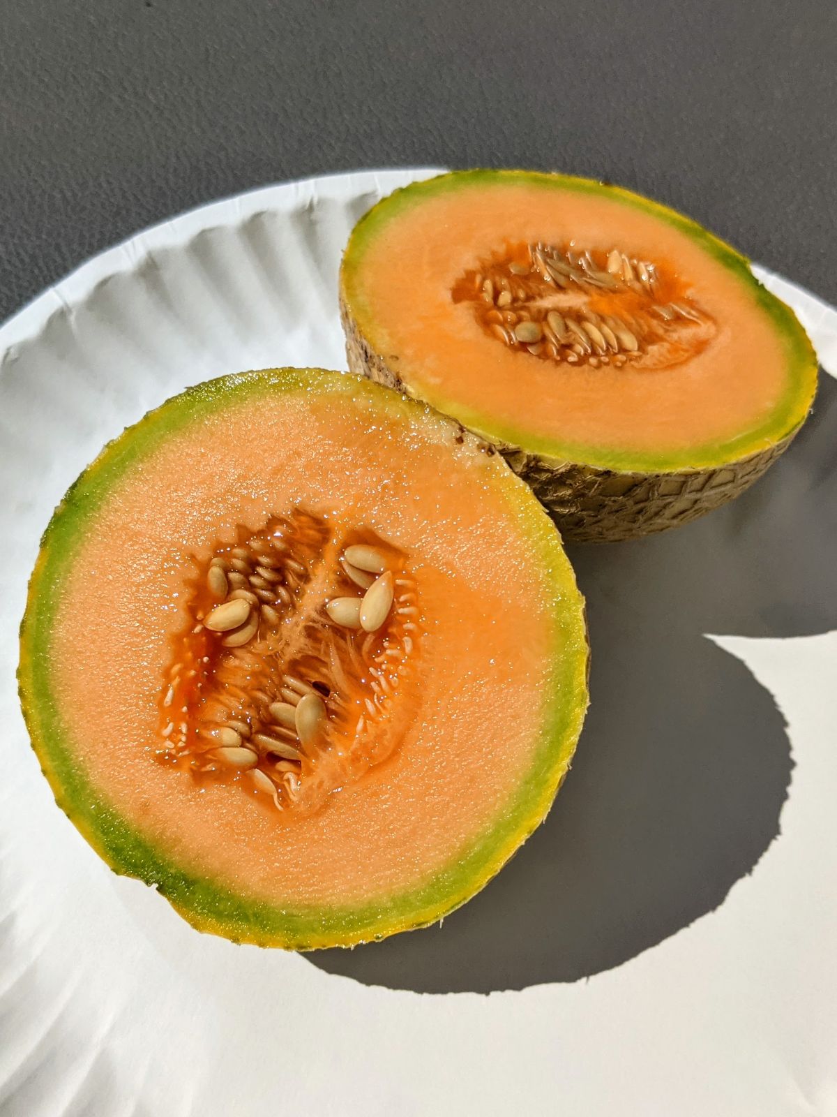Small homegrown cantaloupe cut in half on a white paper plate