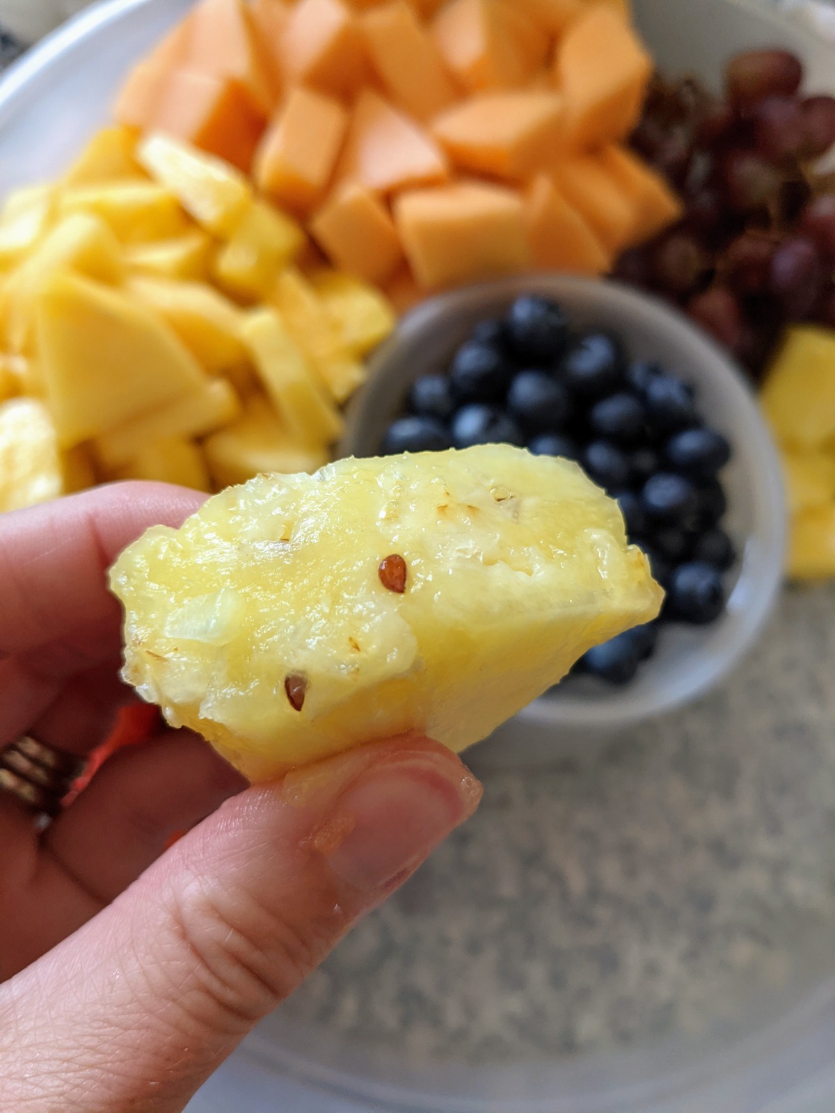 Fresh fruit plate with blueberries, grapes, pineapple and cantaloupe, with pineapple seeds on a chunk