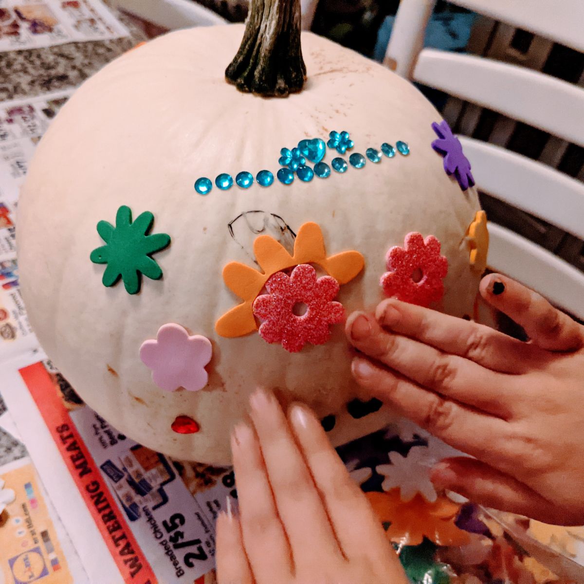 Little hands decorating a white pumpkin with foam flower stickers