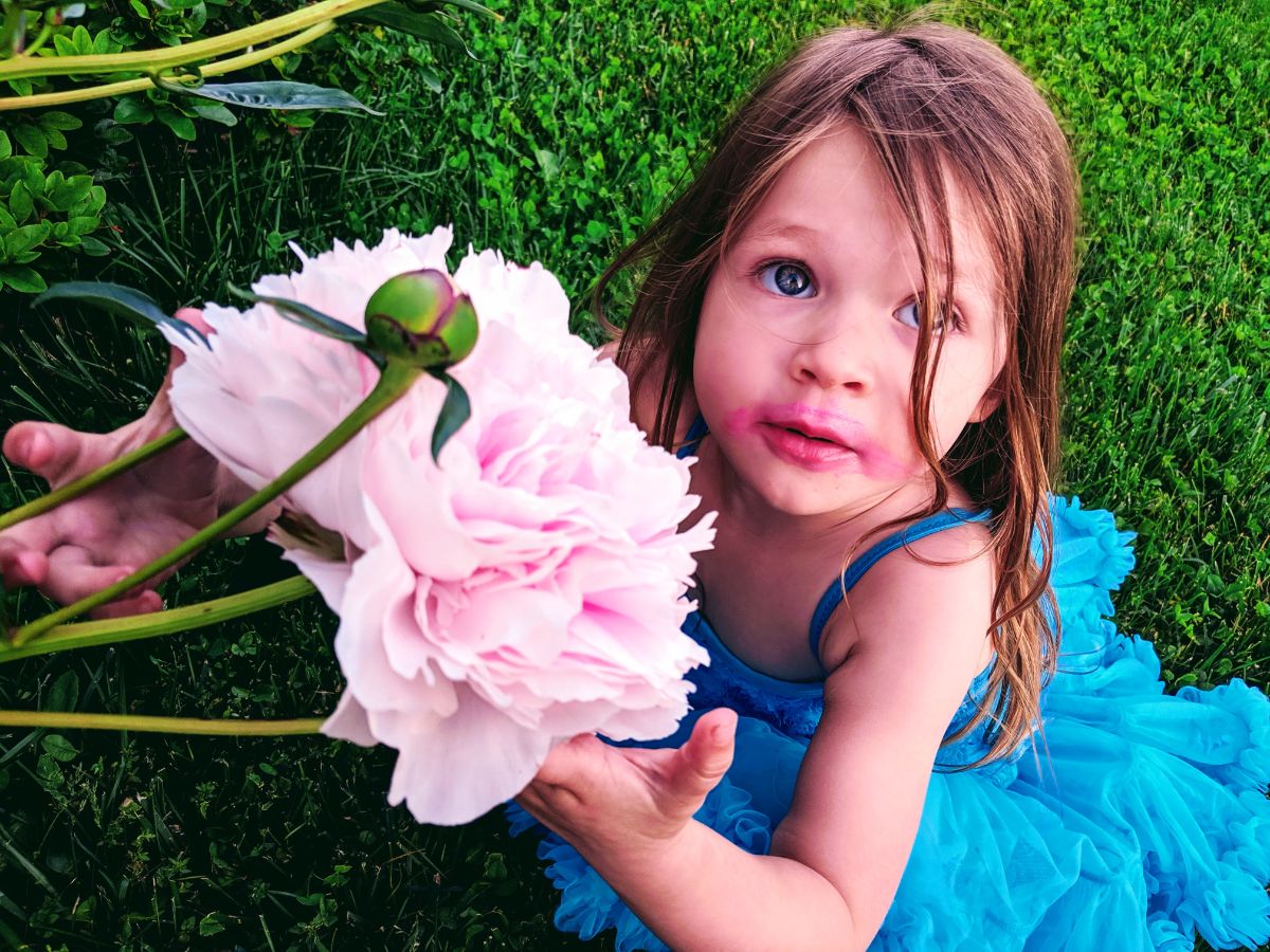 Little girl with lipstick and a pink peony flower