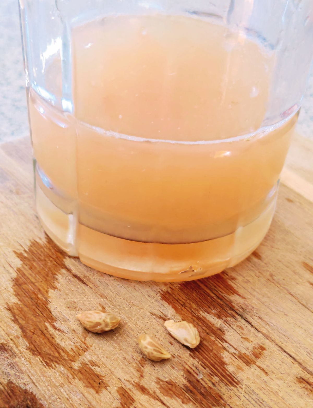 Glass of grapefruit juice and seeds on a cutting board