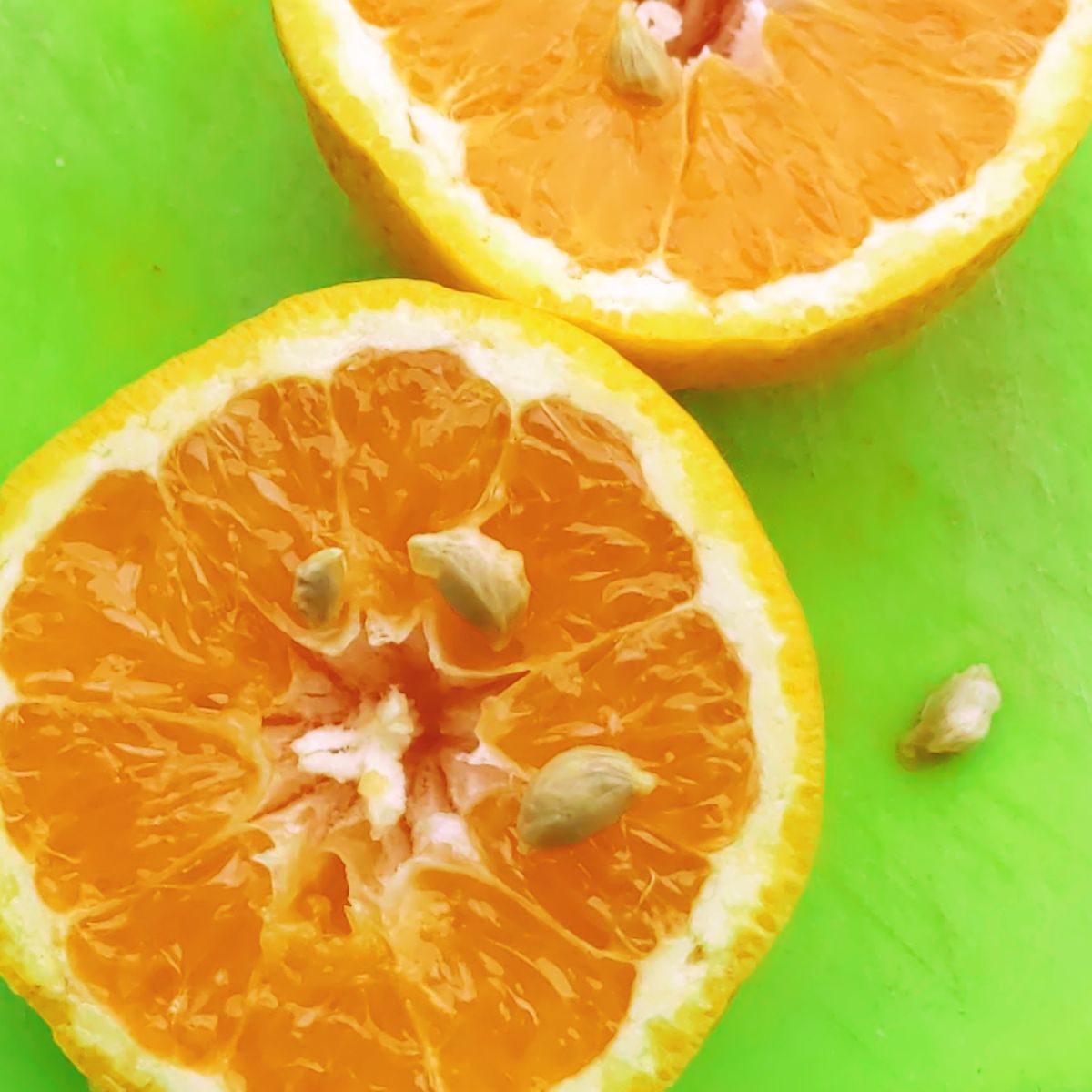 Orange cut open with seeds on green cutting board, two halves