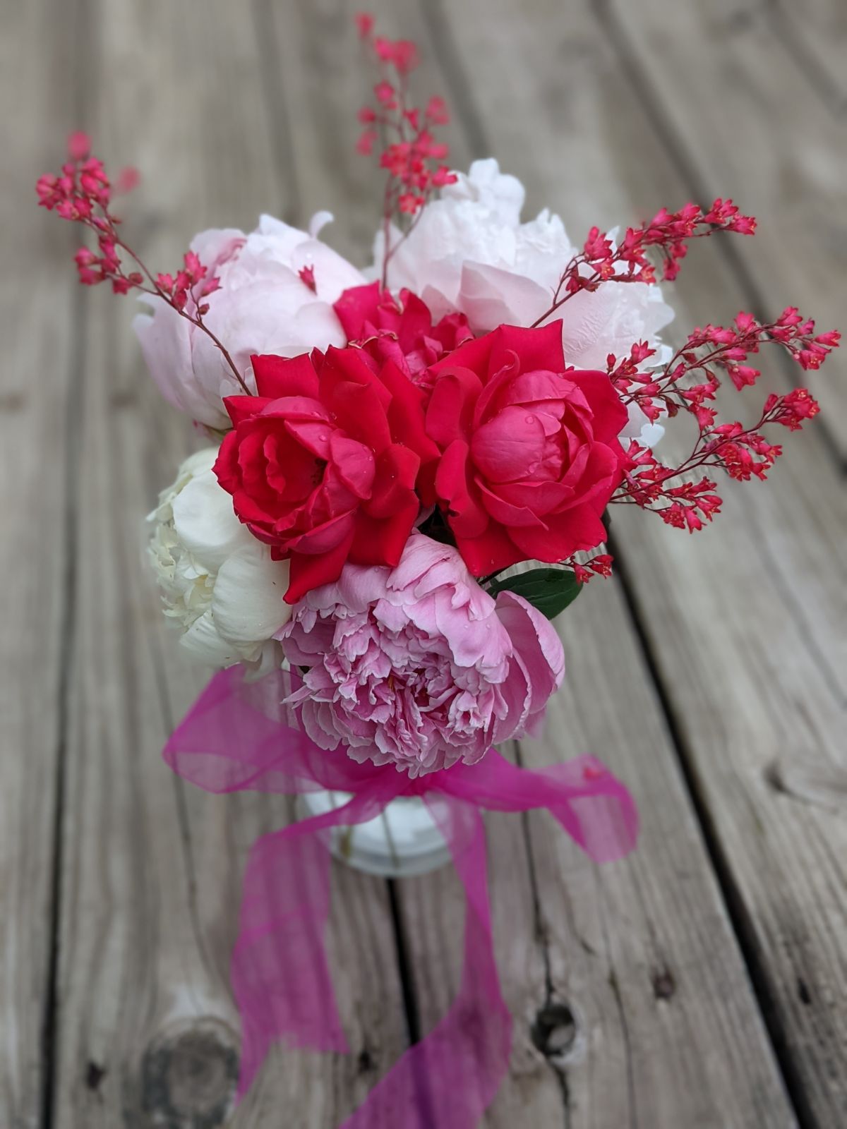 Bouquet of peonies, roses, and coral bells tied with ribbon outside on the deck